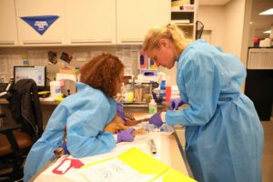 Two female vet techs in blue hospital gowns give a dog chemotherapy.