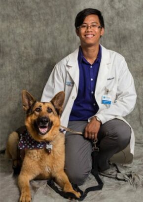 Dr. Laison Nguyen is a resident in our ophthalmology service. He is kneeling next to a large tan and black dog.