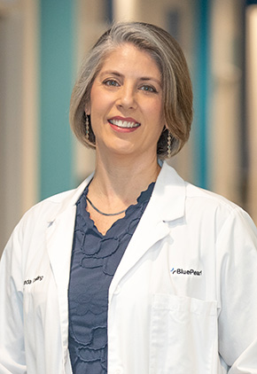 Dr. Amanda Conkling smiling in the lobby of our Grand Rapids hospital. She has on her BluePearl white coat and a navy top.