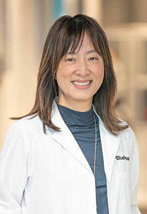 Dr. Yoojin Kim smiling in the lobby of the Grand Rapids hospital. She has on her BluePearl white coat and a blue-grey mock turtle neck.