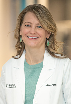 Dr. Gwen Sila smiling in the lobby of the Grand Rapids hospital. She has on her BluePearl white coat and a seafoam green top with matching earrings.