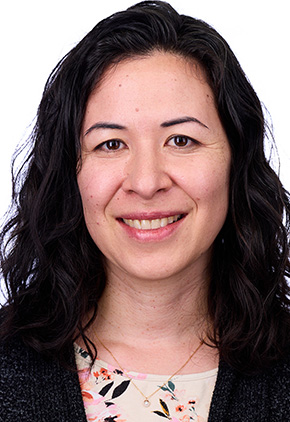 Dr. Laura Stock smiling in front of a white backdrop. She has on a black blazer and abstract floral blouse.