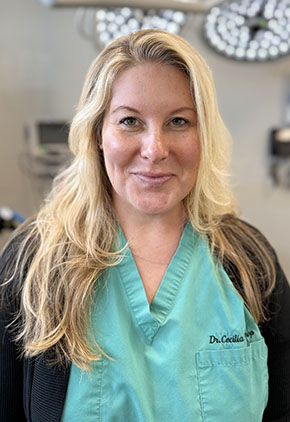 Dr. Cecilia Winthrop smiles in the surgical suite at our hospital. She is wearing seafoam green scrubs and a black cardigan.
