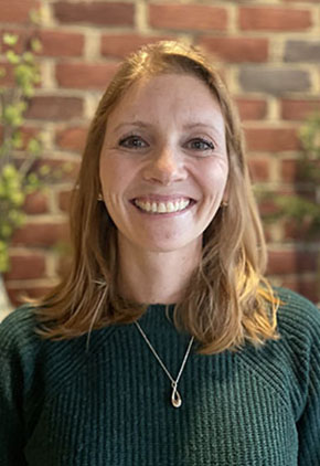 Dr. Alyson Frederick smiles for a headshot in front of a brick wall. She is wearing a forest green sweater and a necklace.