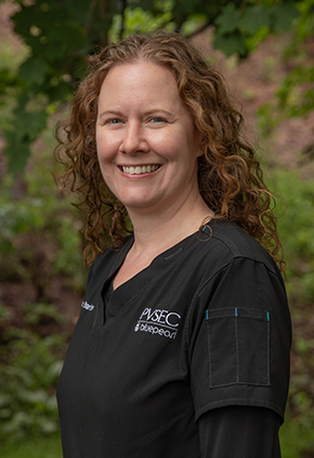 Dr. Shari Brown smiles outside in a lush wooded area. She is wearing black scrubs.