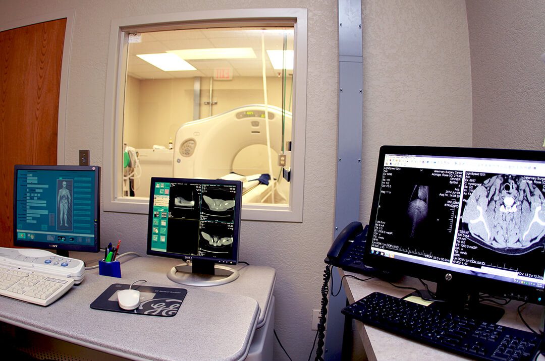 A CT scanner with three computer screens before it.