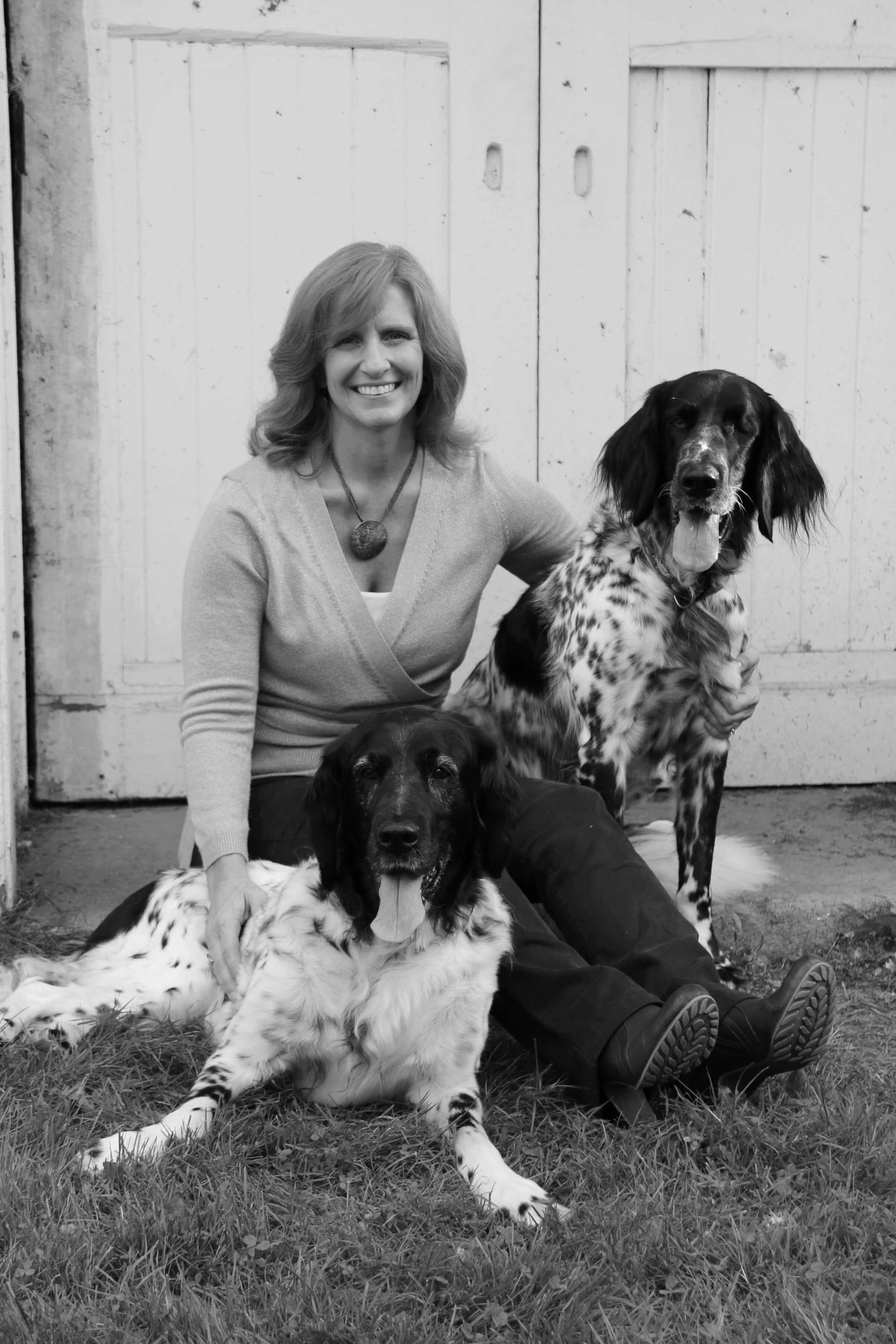 A black and white shot of a woman posing with two large dogs