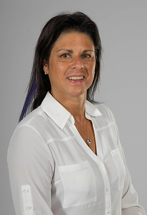 Dr. Danna Torre smiles for a professional headshot in front of a grey studio background. She is wearing a white blouse.