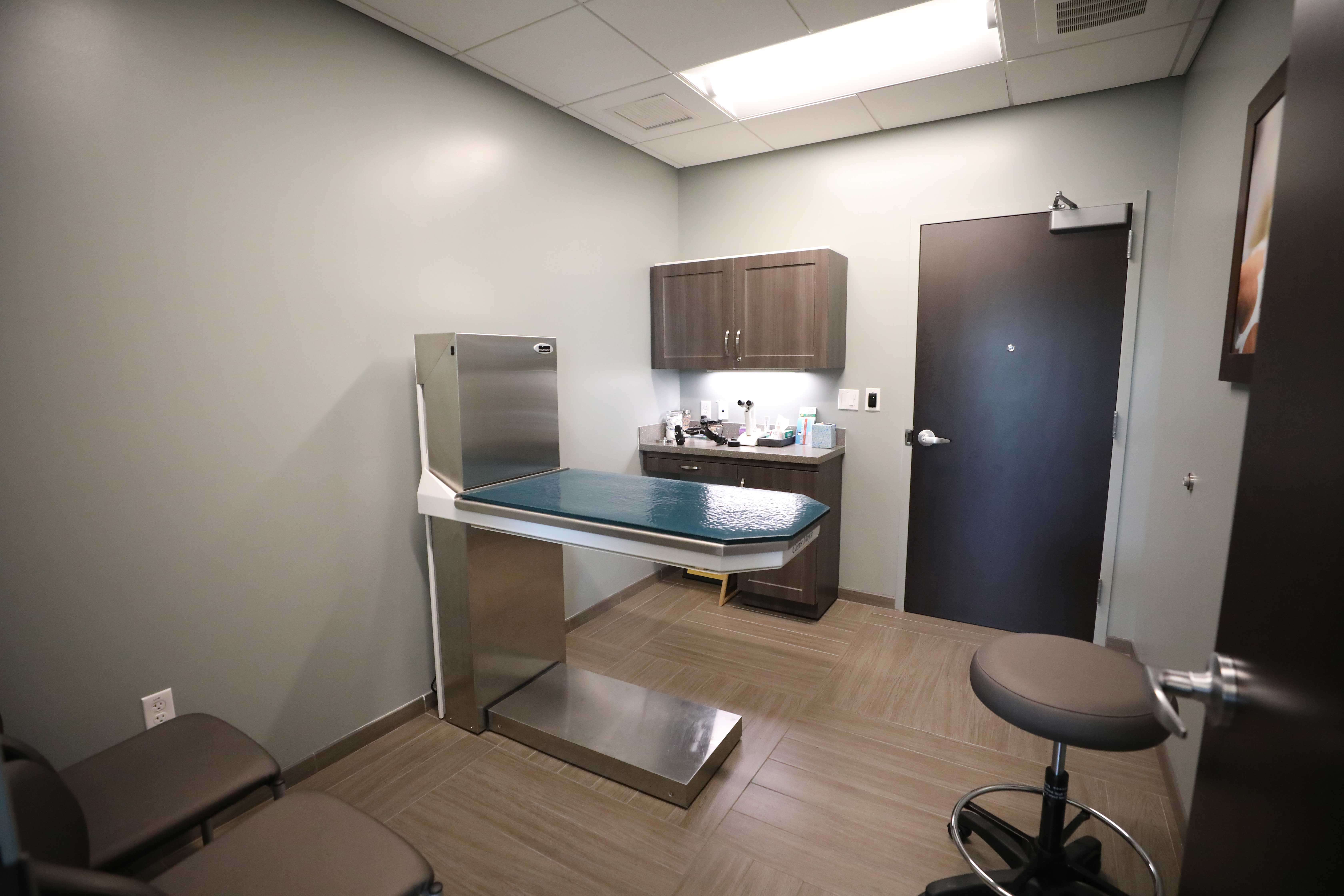 Brightly lit, simply furnished room has a central table for patient examination.