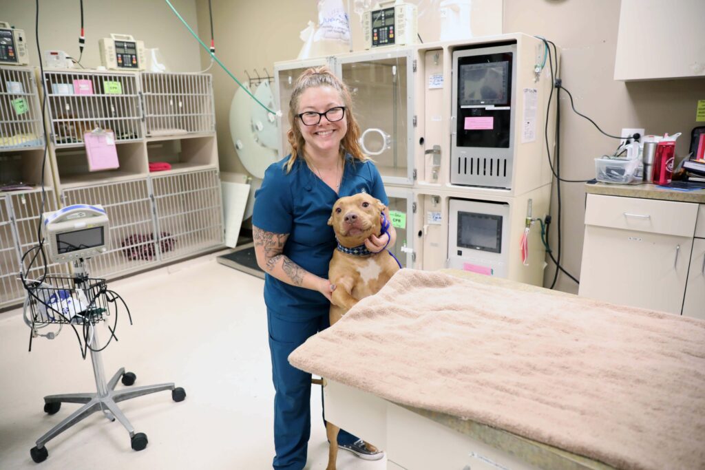 A smiling vet tech stands with a happy dog.
