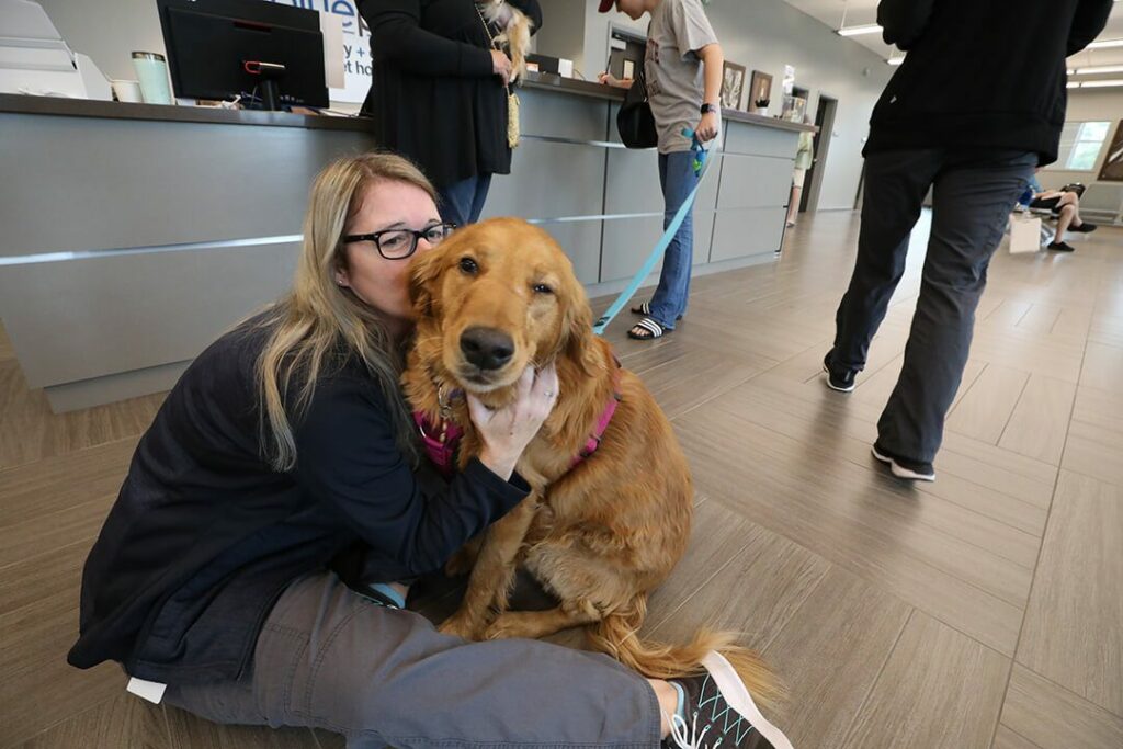 A client care associate sits on the floor with a Golden Retriever and hugs her.