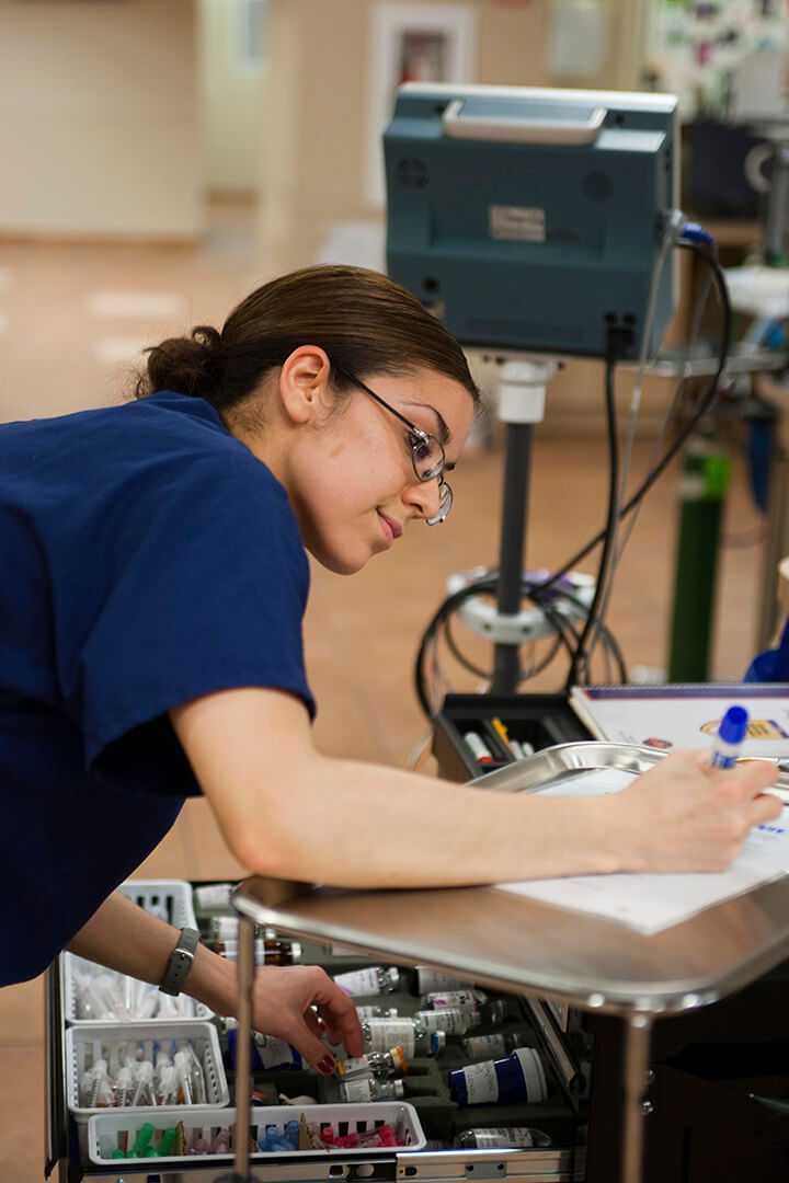 A BluePearl Associate writes something in a ledger while selecting a vital of medication.