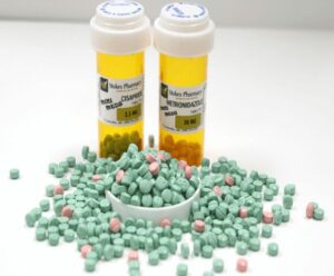 Two medicine bottles on white countertop with a pile of green pills in front. 503B compounding has the potential to change veterinary pharmaceutics. 