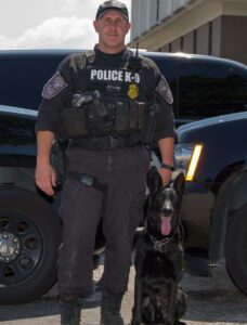 Police K9 handler poses proudly with black K9 officer. 