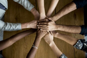 People huddle together with their hands in the center signaling teamwork.