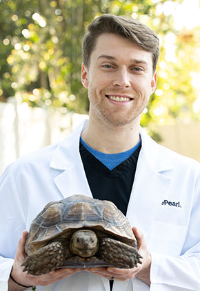 Dr. Toraason outside in his white coat, holding his turtle and smiling.
