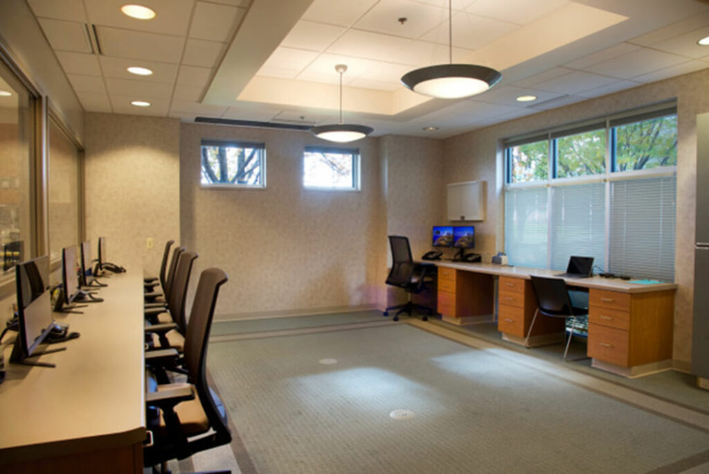 A doctors' station room has desks against the walls with office chairs and computers