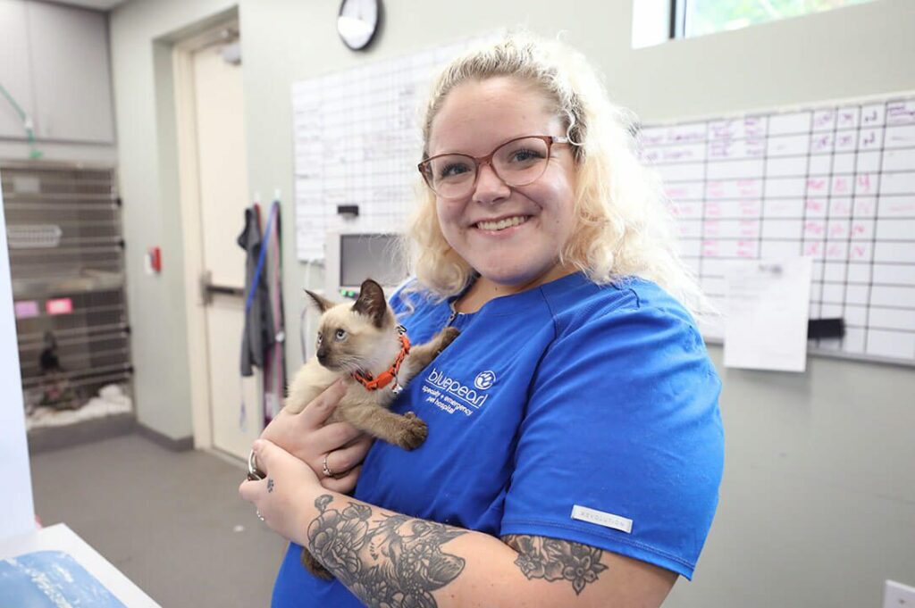 A smiling blond vet tech holds a kitten.