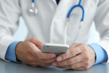 A doctor wearing a white coat checks his smart phone.