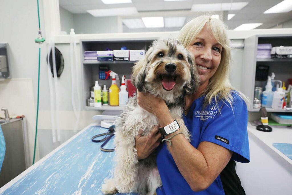 A smiling vet technician poses next to a happy dog.