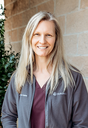 Dr. Jennifer Hamm smiling outside in front of a brick building. She has on maroon scrubs and a grey BluePearl fleece jacket.