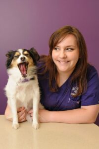 A smiling brunette woman holds a little dog who yawns.