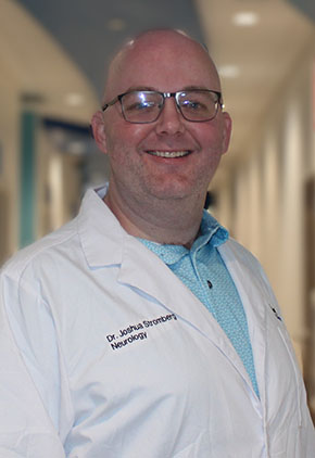 Dr. Joshua Stromberg smiles for a headshot in the lobby of BluePearl Grand Rapids. He is wearing a robin blue dress shirt and his personalized whitecoat.