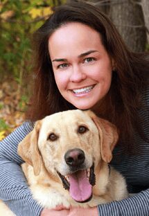 Dr. Elizabeth Breuhl is board certified in veterinary internal medicine. She is hugging a golden Labrador.
