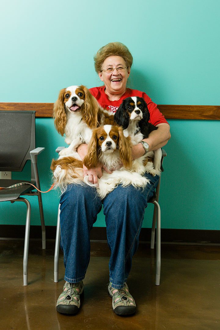 A smiling lady sits with three dogs on her lap.