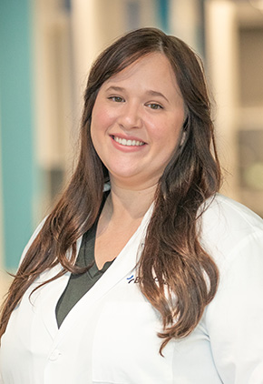 Dr. Danielle Pettifor smiling in the lobby of the Grand Rapids hospital. She has on her BluePearl white coat and a olive green top.