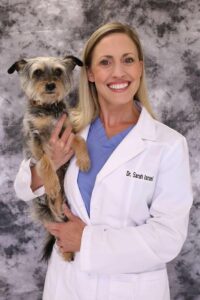 A smiling surgeon in a white coat holds her little dog.