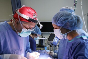Two surgeons in blue gowns operate on a patient.
