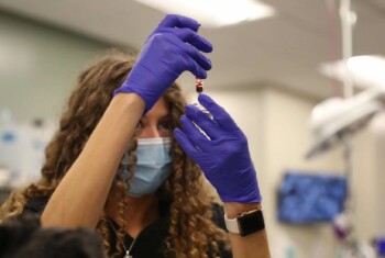 A technician holds a blood sample up with gloved hands.
