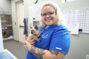 A smiling blond vet technician holds a little kitten.