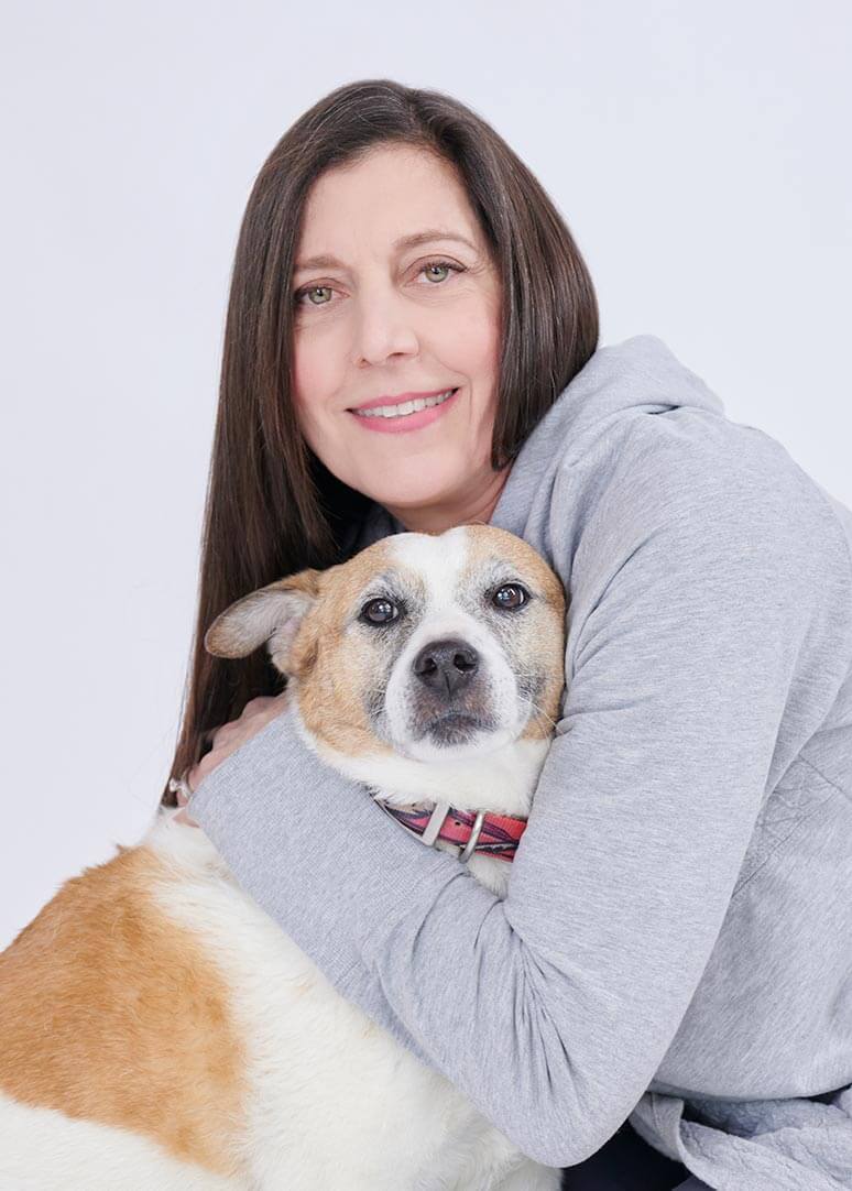 A smiling brunette woman holds a brown and white dog.
