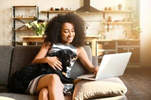 A woman sits on the couch with her dog and her laptop.