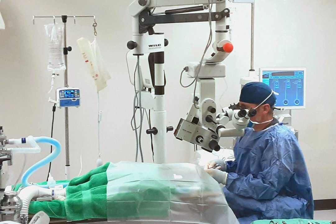 A surgeon looks through a surgical microscope as he works.