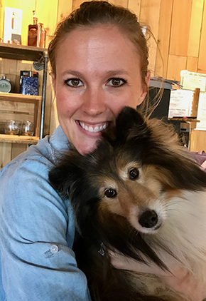 Dr. Susan Shapiro smiling in her kitchen while holding her brown and white border collie in her arms.