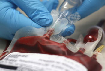 Close up image of gloved hands preparing a bag of donated blood.