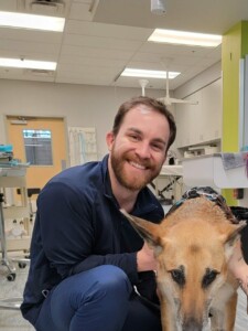 A vet tech poses next to a dog.