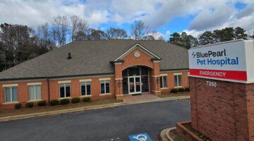 A brick building with windows and a front door is situated behind a marquee sign that reads BluePearl Pet Hospital Emergency.