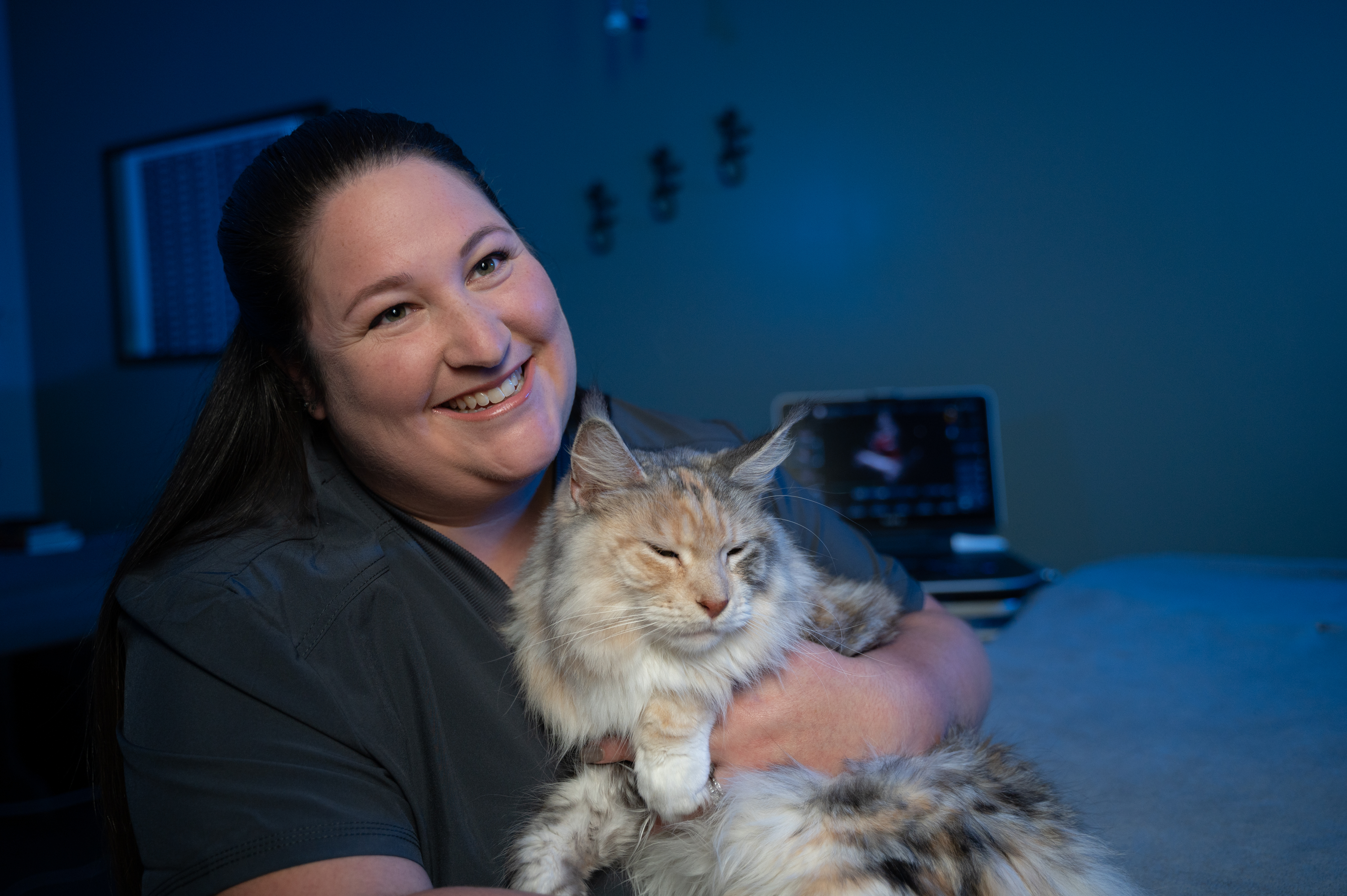 A vet tech snuggles a cat in an exam room.