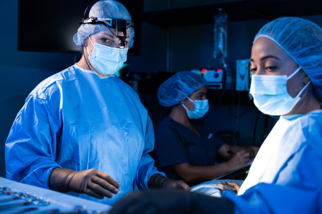 Surgeons wearing scrubs and protective equipment perform a procedure in an operating room.