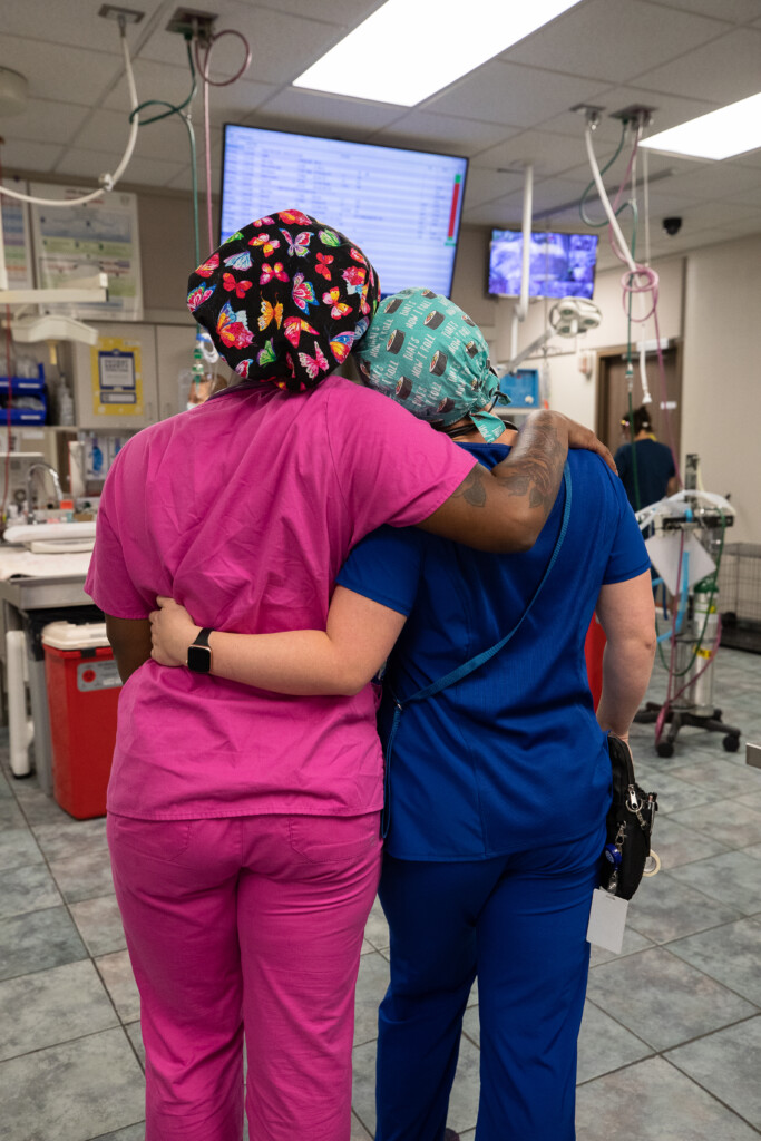 Two technicians in scrubs give each other a side hug in the operating room.