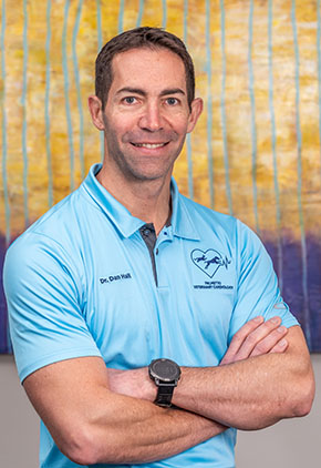 Dr. Daniel Hall smiles in the lobby of our hospital. He is wearing a light blue active polo with his arms crossed across his chest.