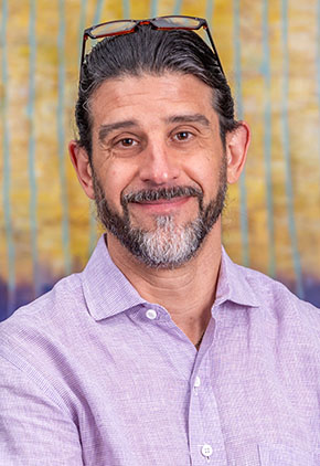 Dr. Tristain Weinkle smiles in the lobby of our hospital. He is wearing a lavender button-up shirt with his arms crossed across his chest.