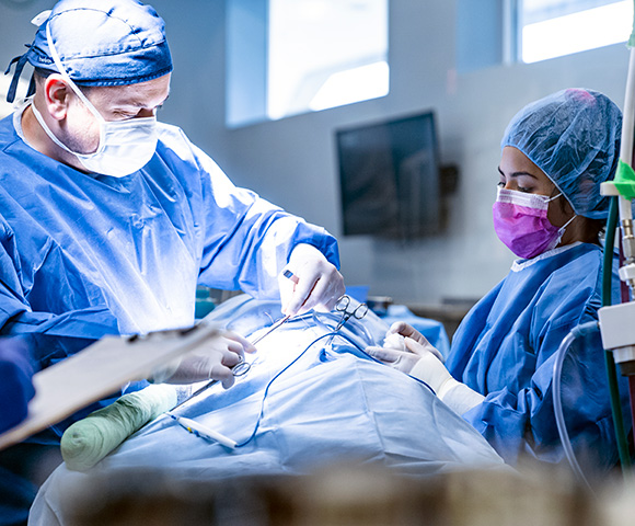 Two surgery Associate wearing scrubs perform surgery on a patient in an operating room.