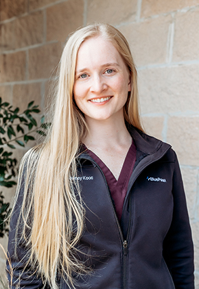 Dr. Lauren Downey-Koos smiling outside in front of a brick building. She has on maroon scrubs and a black fleece BluePearl jacket.