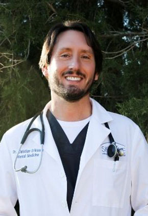 BluePearl's board certified internist, Dr. Christian Eriksson, smiling outside in his lab coat with a stethoscope around his neck.
