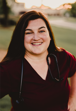 Dr. Jill Western, smiling outside while wearing maroon scrubs and a stethoscope around her neck.